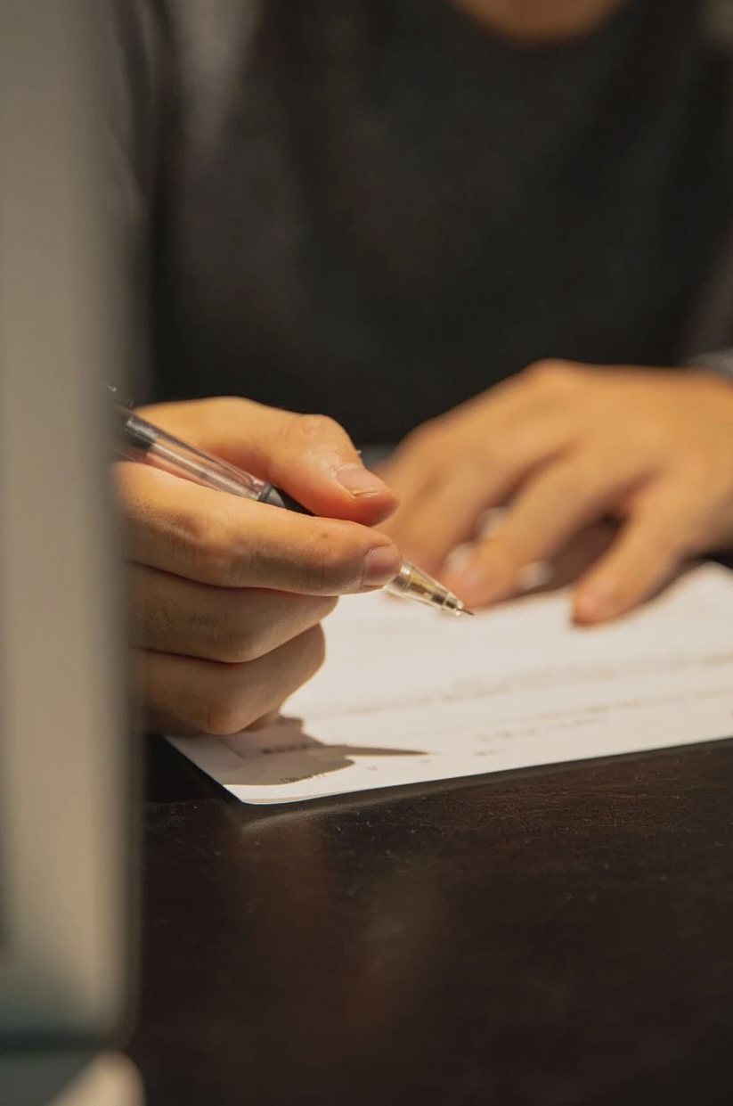 Person's hands signing a paper document at a dark desk